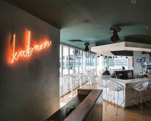 A modern bar interior with a neon sign reading "kabasa," featuring white chairs and a sleek counter.
