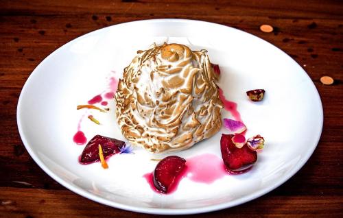 A beautifully plated dessert resembling a meringue dome, garnished with strawberries and colorful flower petals.