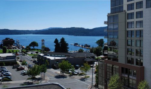 A scenic view of a lake with a dock, surrounded by trees and buildings, under a clear blue sky.