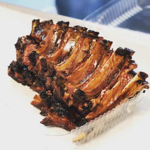 A delicious rack of grilled ribs with a caramelized glaze, resting in a clear plastic container.