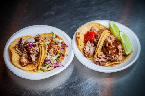 Two plates of tacos: one with shredded meat and cabbage, the other with meat, salsa, and lime wedges.