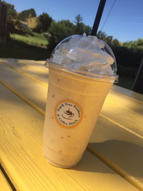 A creamy smoothie topped with whipped cream, served in a clear cup on a yellow table, with a scenic background.