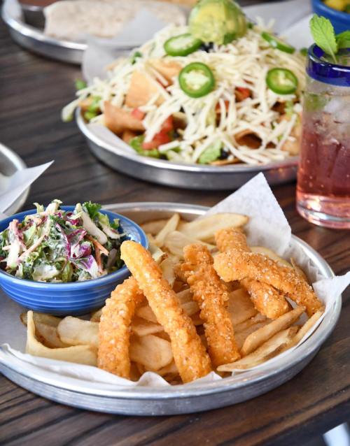 A plate of crispy fries and golden onion rings, served with a side of coleslaw and a colorful drink in the background.