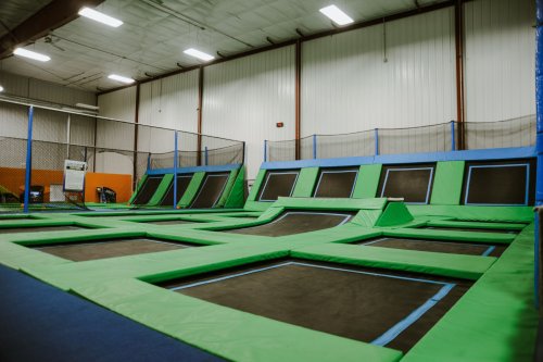 Indoor trampoline park featuring multiple green trampolines and safety nets in a spacious facility.