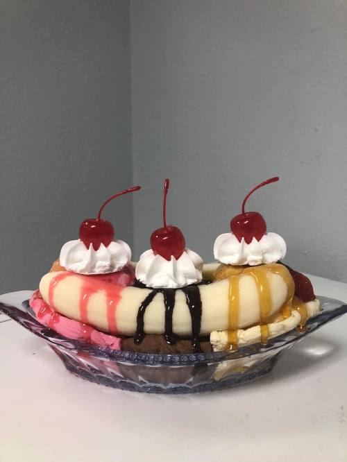 A colorful banana split topped with whipped cream and cherries, served in a glass dish.