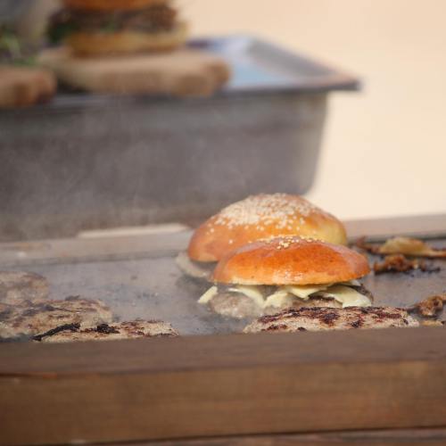 Grilling burgers on a hot griddle, with sesame seed buns and melted cheese, surrounded by steam and sizzling patties.