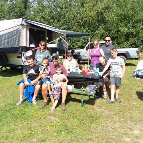 A group of people gathered around a picnic table at a campsite, smiling and enjoying their time together.