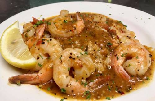 A plate of shrimp in a savory sauce, garnished with parsley and a lemon wedge.