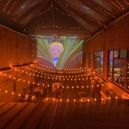A cozy restaurant with string lights and a large projection of a cartoon character on a wall.