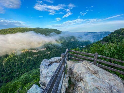 A scenic view from a rocky overlook, with lush green hills and misty valleys under a blue sky.