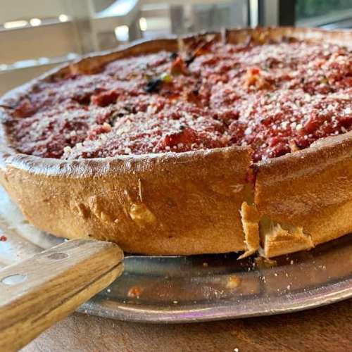 A close-up of a deep-dish pizza on a metal tray, topped with tomato sauce and sprinkled with cheese.