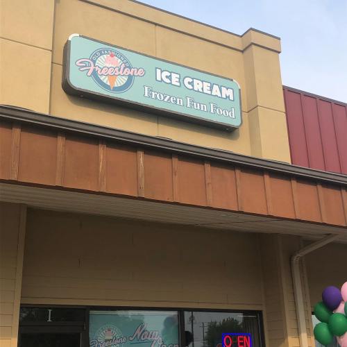 Sign for "Freestone Ice Cream" featuring "Frozen Fun Food" above a storefront with colorful balloons.