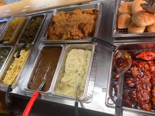 A buffet spread featuring fried chicken, mashed potatoes, green beans, macaroni and cheese, rolls, and barbecue ribs.