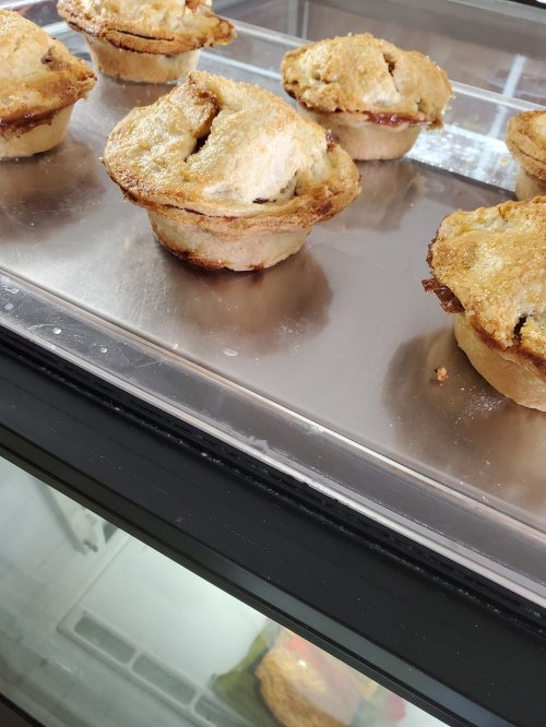 Freshly baked mini pies with golden crusts displayed in a glass case.
