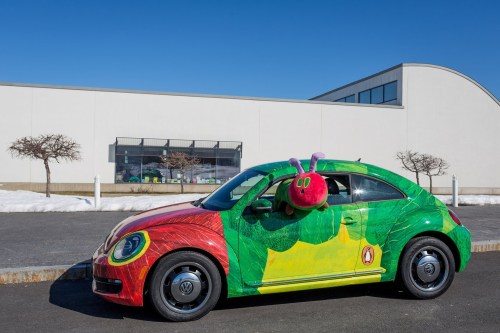 A colorful car decorated like a caterpillar, with a large caterpillar head on the roof, parked outside a building.