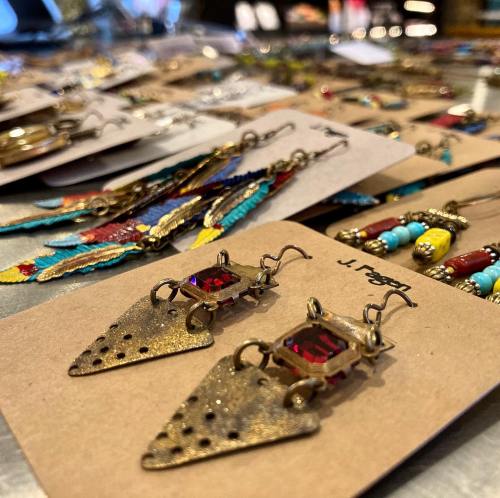 Close-up of unique earrings with red gems, displayed among various colorful jewelry pieces on a table.