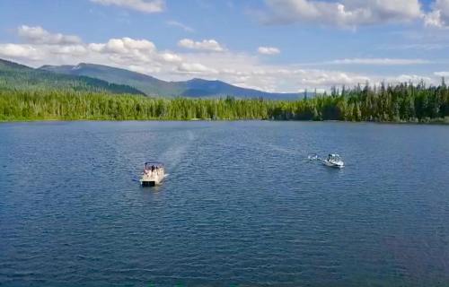 Two boats navigate a serene lake surrounded by lush green forests and mountains under a blue sky with fluffy clouds.