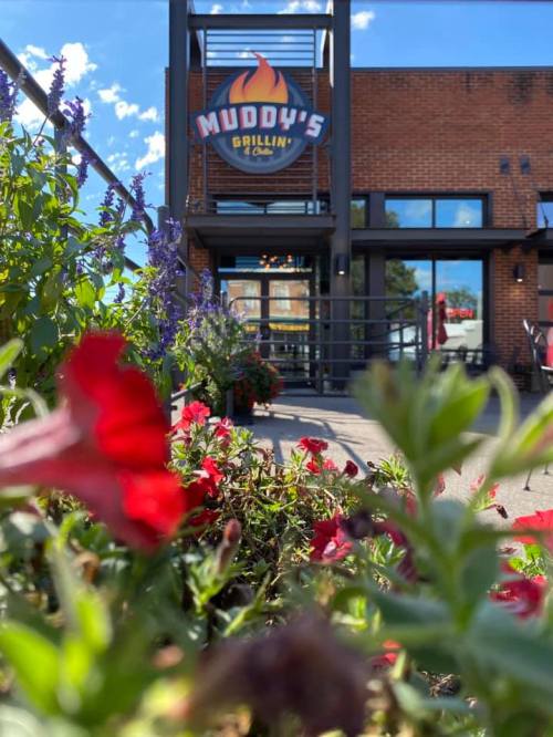 A view of Muddy's Grillin' & Cafe, framed by colorful flowers in the foreground and a clear blue sky above.