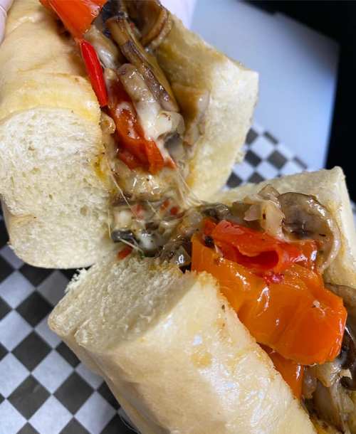 A close-up of a cheesy sandwich filled with sautéed mushrooms and red peppers, held in two hands.
