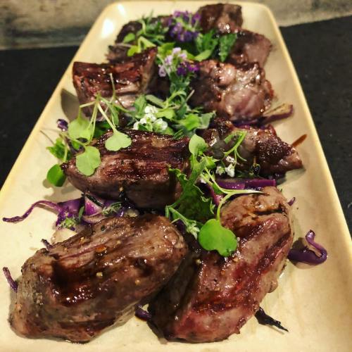 A platter of grilled meat garnished with fresh herbs and purple cabbage, showcasing a delicious presentation.