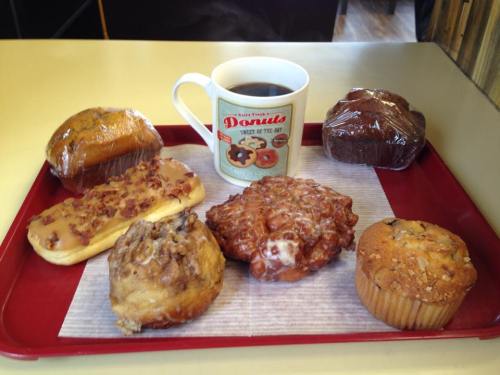 A red tray with a variety of pastries and a cup of coffee, including donuts, muffins, and a cinnamon roll.