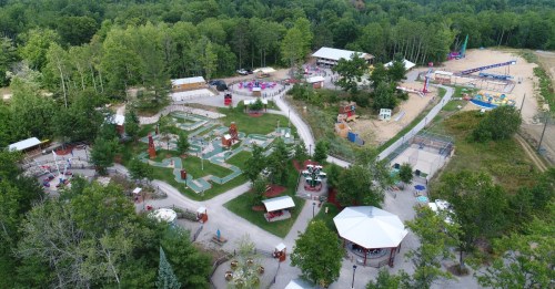 Aerial view of a recreational park featuring mini-golf, play areas, and various attractions surrounded by trees.