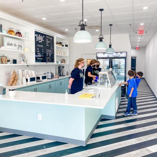 Two staff members serve customers at a bright ice cream shop with a modern design and striped flooring.