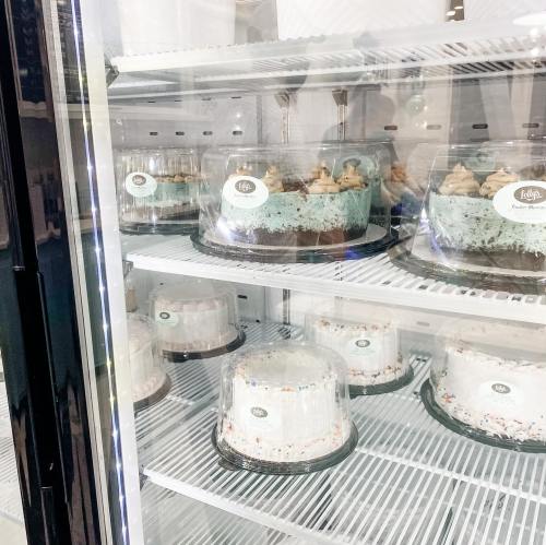 A display case filled with various cakes, including layered and frosted options, in a refrigerated unit.