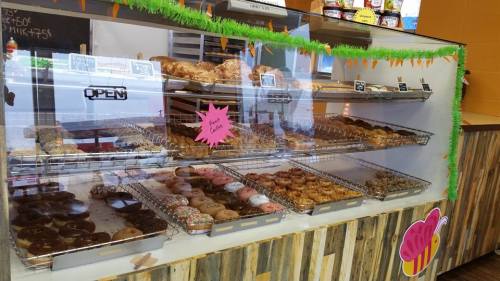A display case filled with various donuts, including glazed, sprinkled, and filled options, in a colorful bakery setting.