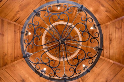 A decorative circular chandelier with intricate metalwork, hanging from a wooden ceiling.