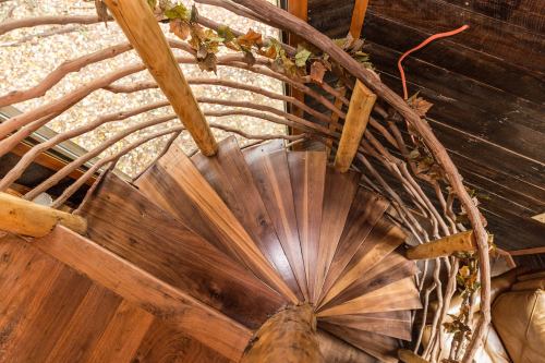 A spiral wooden staircase with a natural wood railing adorned with leaves, viewed from above.