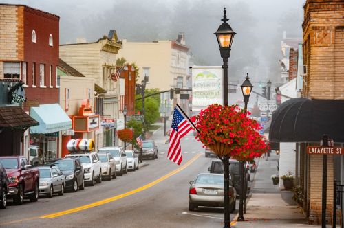 A foggy street scene in a small town, featuring shops, parked cars, and an American flag hanging from a lamppost.