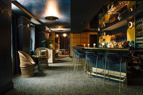 A stylish bar interior featuring a blue color scheme, elegant seating, and a well-stocked bar with ambient lighting.