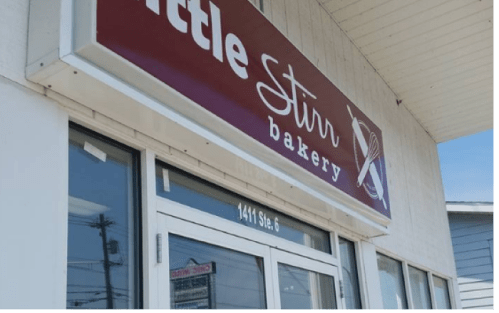 Sign for "Little Stir Bakery" displayed above the entrance of a bakery, with a clear blue sky in the background.