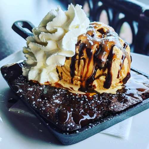 A warm brownie topped with ice cream, whipped cream, and drizzled with caramel sauce, served in a small skillet.
