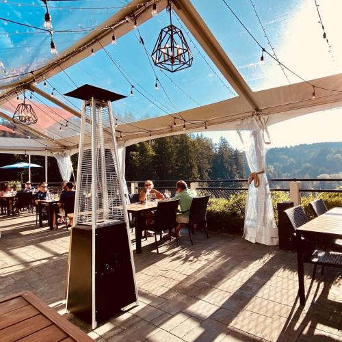 A sunny outdoor dining area with string lights, a heater, and guests enjoying their meals under a tent.