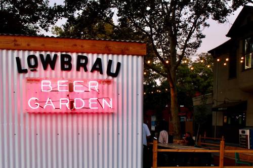 Neon sign reading "Lowbrau Beer Garden" in a lively outdoor setting with string lights and trees.