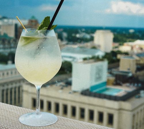 A refreshing cocktail with mint and lime sits on a table, overlooking a city skyline in the background.