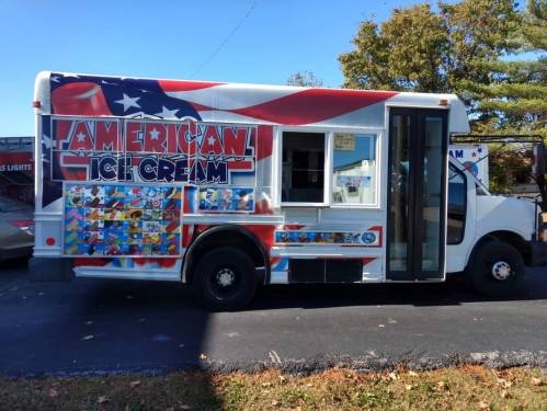 A colorful ice cream truck with an "American Ice Cream" sign and various ice cream images on the side, parked on a street.