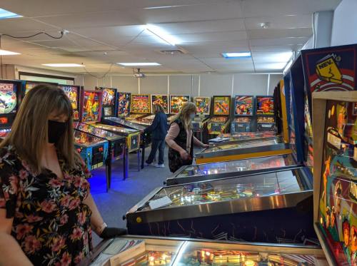 Two women play pinball machines in a brightly lit arcade filled with various pinball games.