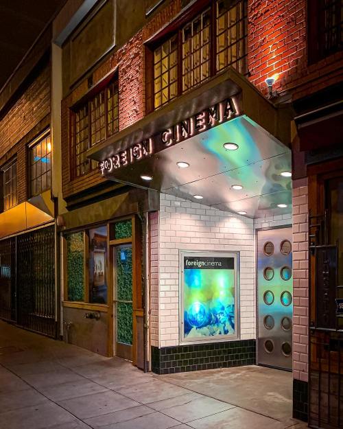 Entrance of Foreign Cinema restaurant, featuring a lit sign and modern design, set against a nighttime urban backdrop.