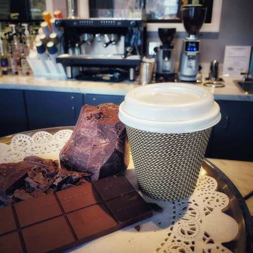 A tray with chocolate pieces and a coffee cup in a café setting, with an espresso machine in the background.