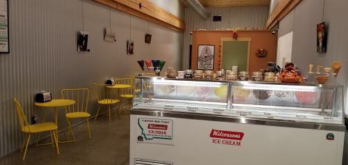 A cozy ice cream shop featuring a display of colorful ice cream flavors and yellow seating.