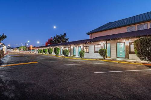 A well-lit motel exterior at dusk, featuring green doors and neatly trimmed hedges along a paved parking area.