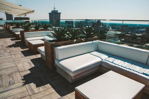 Rooftop lounge area with white seating and potted plants, overlooking a city skyline on a sunny day.