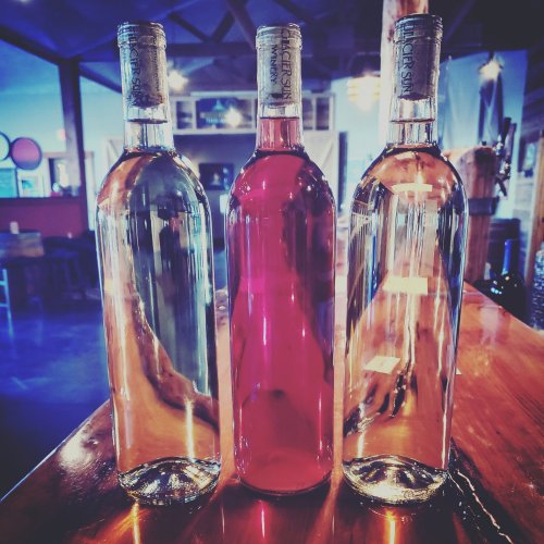 Three wine bottles on a wooden table: one clear, one pink, and one light amber, with a rustic background.