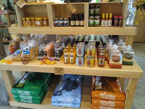 A wooden shelf displaying various food products, including oils, sauces, pasta, and snacks, arranged neatly.