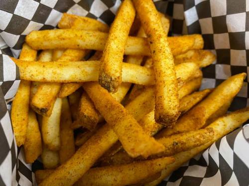 A basket of golden French fries seasoned with spices, resting on a black and white checkered paper.