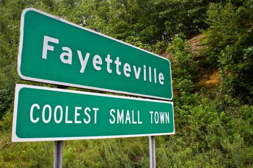 Green road sign indicating "Fayetteville" and "Coolest Small Town" with greenery in the background.