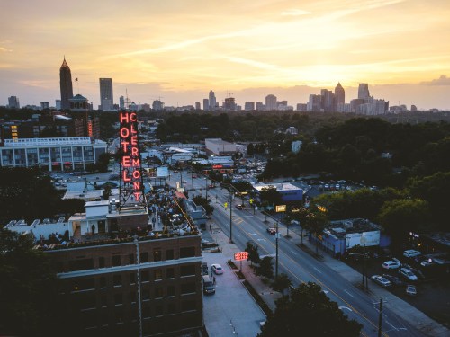 Aerial view of a city skyline at sunset, featuring the neon sign of the Hotel Clermont and bustling streets below.
